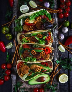 several tacos are lined up on a tray with tomatoes, avocado and other ingredients