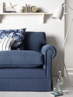 a blue couch sitting in front of a white wall with shelves on either side and a lamp next to it