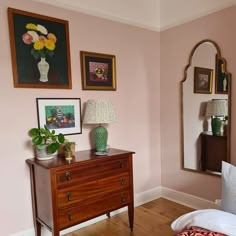 a bedroom with pink walls and pictures on the wall, including a chest of drawers