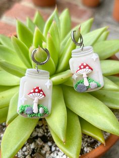 two glass jars with mushrooms on them are sitting in a flower pot next to some plants