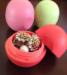 three plastic containers with jewelry in them sitting on a table next to some balls and beads