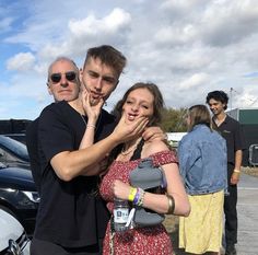 two people standing next to each other in front of parked cars and one person covering his mouth