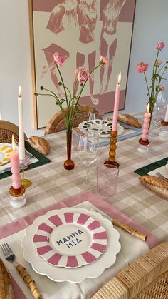 the table is set with pink and white plates, candles, and flowers in vases