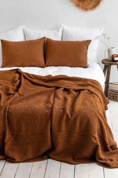 a bed with brown blankets and pillows on top of it in a bedroom next to a wooden table