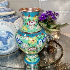 two vases sitting on top of a glass table next to flowers and other decorative items