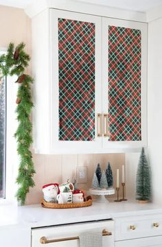 Transform your kitchen for the holidays! This DIY guide shows how to decorate white kitchen cabinets with festive red and green plaid wrapping paper, creating a cozy Christmas vibe. Add a pinecone-studded green garland to your window frame, and style your countertop with holiday mugs, bottle brush trees, and elegant candlesticks for a stunning seasonal look. Perfect for a festive kitchen refresh! Wrapped Cabinets Christmas, Wrapped Cabinets, Christmas Cabinets, Plaid Wrapping Paper, Holiday Mugs