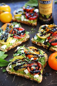 several slices of bread with tomatoes, black olives, and cheese on them next to a bottle of wine