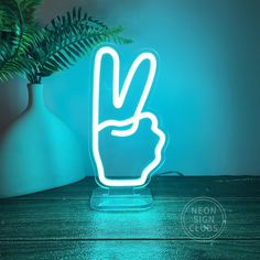 a neon sign with a peace hand in front of a potted plant on a table