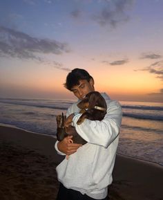 a man holding a dog on the beach at sunset