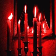 candles are lit in front of a mirror with red light coming from the candle holders