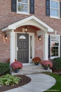 the front porch is decorated with flowers and potted plants on either side of the door