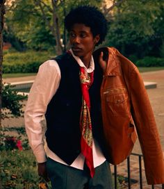 a young man wearing a red tie and vest standing next to a brown leather jacket