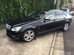 a black mercedes c - class is parked on the side of the road in front of some bushes