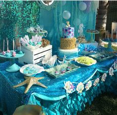 the table is set up for a little mermaid birthday party with blue and green decorations