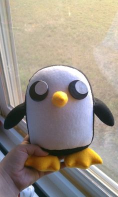 a stuffed penguin sitting on top of a window sill next to a person's hand