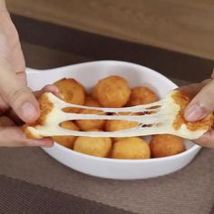 two hands holding up a piece of food in a white bowl on top of a table