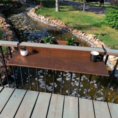 two coffee cups are sitting on a wooden table next to a river with rocks in it