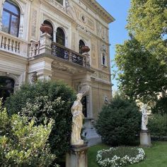 a large building with statues in front of it and bushes around the yard area on either side