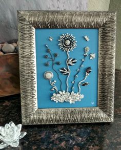 a silver and blue frame with some flowers on the wall in front of it, next to a small white flower