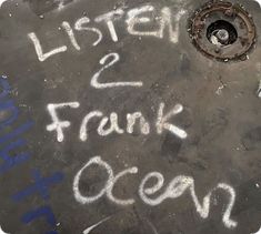 the words listen and frank ocean written in white chalk on an asphalt surface with a drain