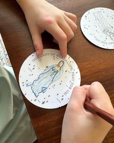 a child is drawing on a paper plate with a pen and pencil while another person holds their hand over it