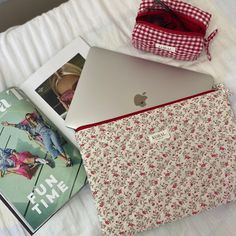 an open laptop computer sitting on top of a bed next to a book and purse