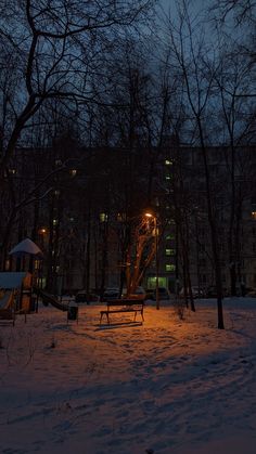 a bench in the middle of a snowy park at night with lights shining on it