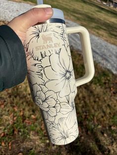 a person holding a travel mug with flowers painted on the front and side of it