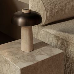 a table lamp sitting on top of a block of concrete next to a couch in a living room