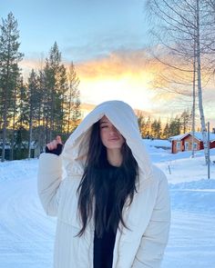 a woman standing in the snow wearing a white jacket and black top with hood up