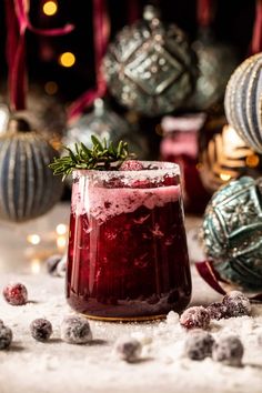 a glass filled with red liquid surrounded by christmas ornaments and baubles in the background