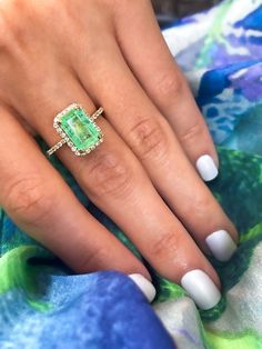 a woman's hand with a green ring on top of her finger and white nails