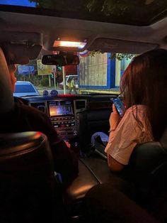 a man and woman sitting in the driver's seat of a car looking at their cell phones