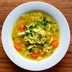 a bowl of chicken noodle soup with carrots and parsley