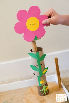 a person holding up a flower made out of toilet paper on top of a wooden stand