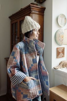 a woman standing next to a window wearing a coat and hat with an overcoat on