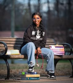 a woman sitting on a park bench with her dog leashed to the ground next to books