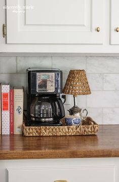 a coffee maker and some books on top of a kitchen counter in front of white cabinets