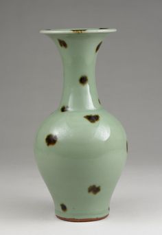 a green vase with brown spots on the top and bottom, sitting against a gray background