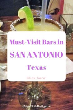 a close up of a drink in a glass on a table with a sign that says must visit bars in san antonio texas