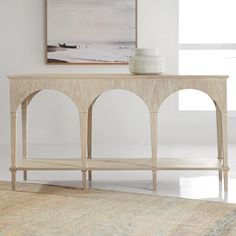 a white vase sitting on top of a wooden table in front of a painting and rug