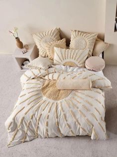 a bed with white and gold comforters in a bedroom next to a nightstand filled with vases