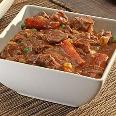 a white bowl filled with meat and veggies on top of a woven place mat