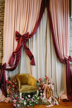 a chair sitting in front of a window covered with pink curtains and flowers on the floor