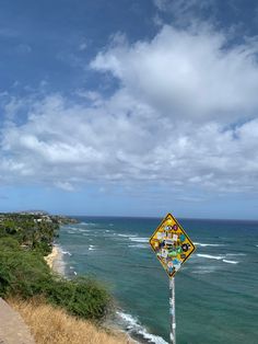 a yellow and black street sign sitting on the side of a cliff near the ocean