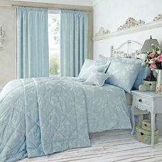 a bed with blue comforters and pillows in a bedroom next to a window filled with pink flowers