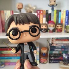 a hand holding a harry potter figurine in front of bookshelves and shelves