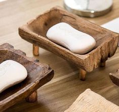 three soaps in wooden trays on a wood table next to towels and a clock