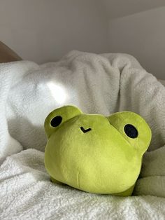 a green frog stuffed animal laying on top of a white bed sheet with black eyes