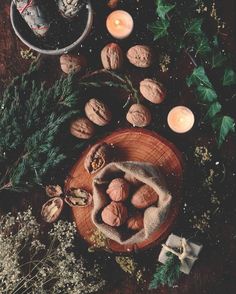 some nuts are sitting on a wooden plate with candles and greenery around it in front of a teapot